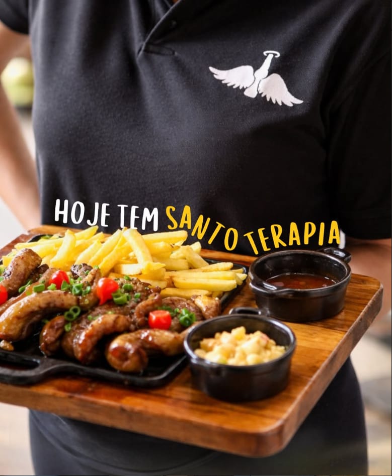Garçom servindo uma tábua de linguiça, fritas e molhos com a camisa do Santo Grau